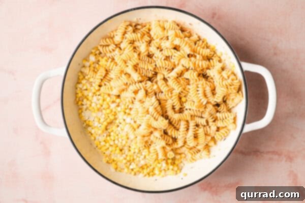 Cooked pasta combined with the sautéed corn and onion mixture in a pan.