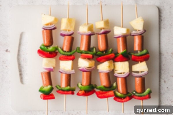 Sizzling Skewer Dogs 4 Hot dog, pineapple, and bell pepper pieces expertly threaded onto wooden skewers, ready for grilling.