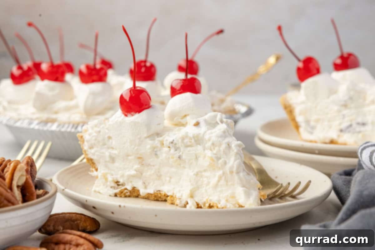 Close-up of a slice of Million Dollar Pie on a plate, topped with whipped cream and a cherry, with the full pie in the background.