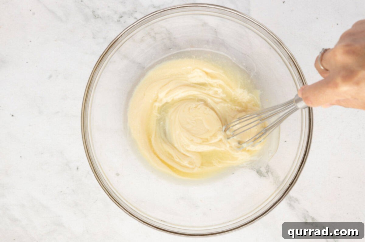 Hand whisking sweetened condensed milk and lemon juice together in a glass mixing bowl.