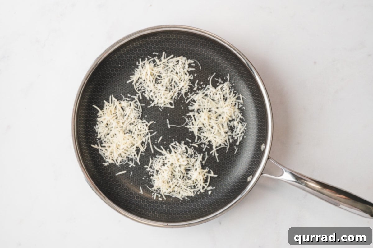 Crispy Cheese Eggs 4 A nonstick skillet with piles of shredded cheese melting into round mounds to form frico nests.