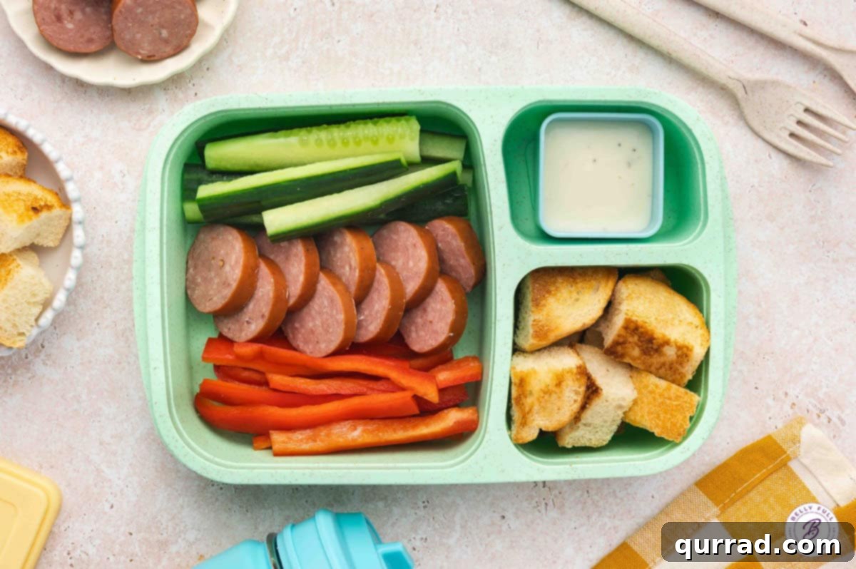 Delicious & Easy School Lunches 11 Bento box lunch with toasted bread cubes, red bell pepper sticks, cucumber slices, sliced Kielbasa, and creamy Ranch dressing for dipping.