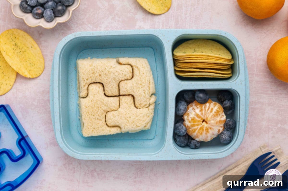 Delicious & Easy School Lunches 4 Bento box lunch featuring a crustless puzzle-cut sandwich, crispy chips, and fresh fruit for a playful meal.