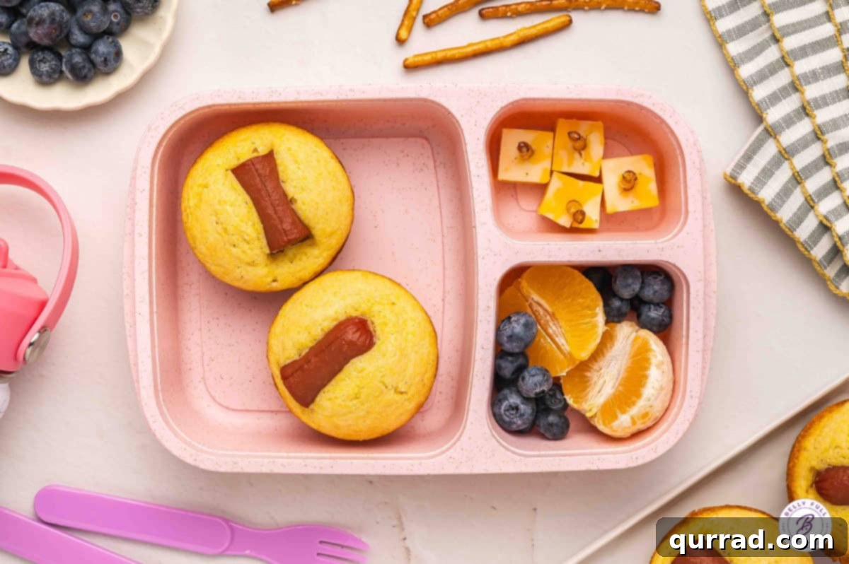 Delicious & Easy School Lunches 7 School lunch bento box featuring homemade corn dog muffins, cubed cheese with pretzel sticks, and fresh fruit.
