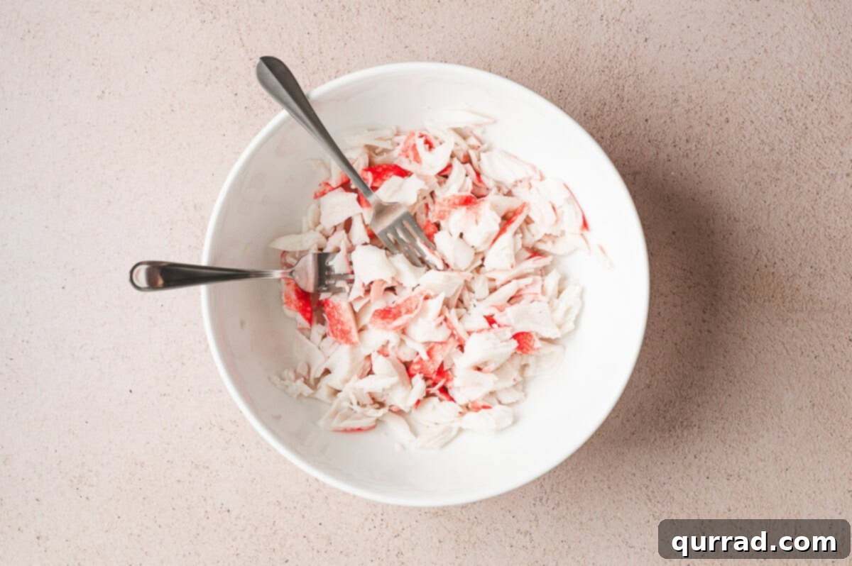 Signature Crab Salad 4 Flaked imitation crab meat in a large bowl with two forks, ready for preparation.