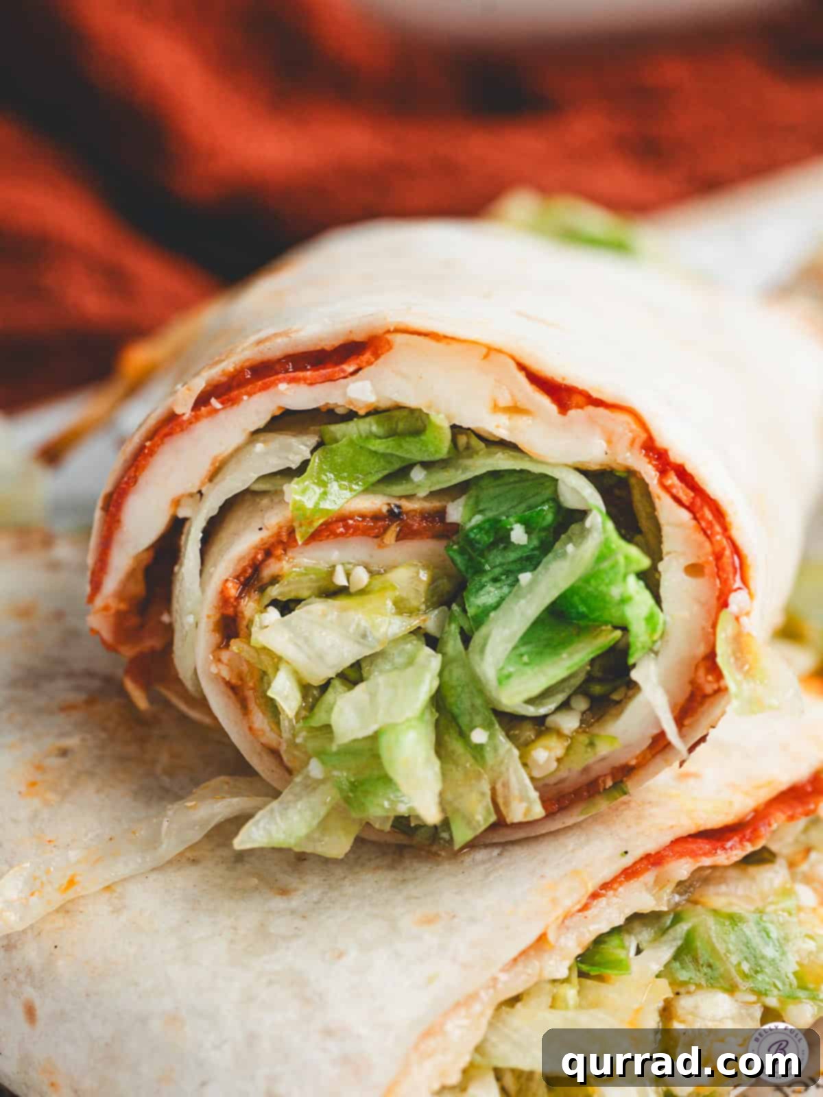 Pizza Garden Wrap 2 Rolled pizza salad wrap sliced to show layers of melted cheese, pepperoni, and lettuce filling.