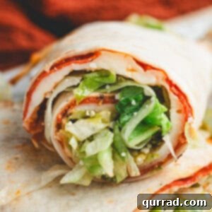 Rolled pizza salad wrap sliced to show layers of melted cheese, pepperoni, and lettuce filling.