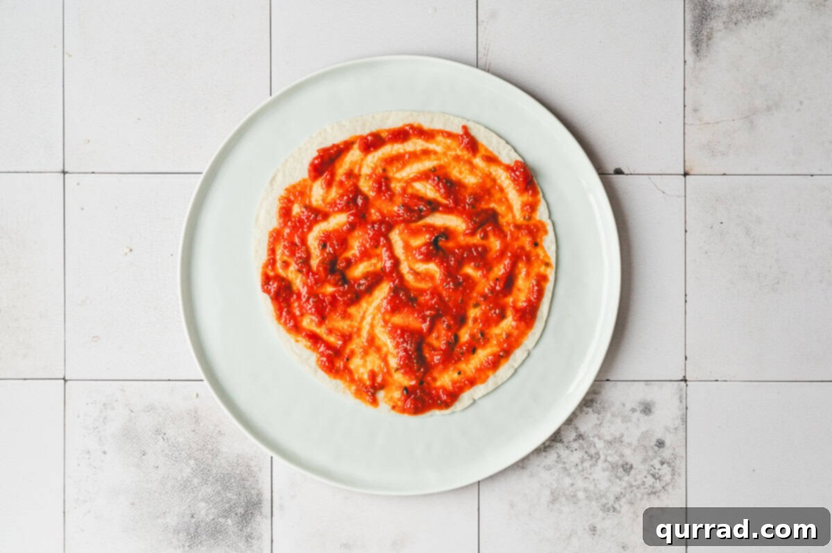 Pizza Garden Wrap 5 Flour tortilla on a plate spread with marinara sauce in an even layer.