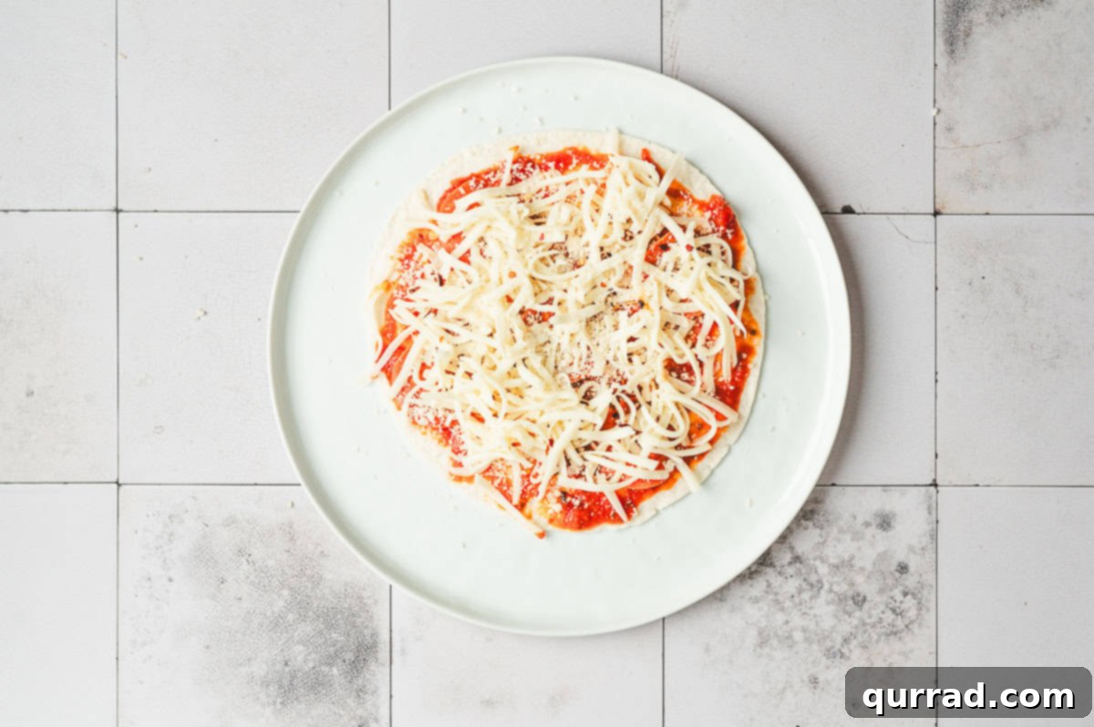 Pizza Garden Wrap 6 Tortilla topped with marinara sauce, shredded mozzarella, and Parmesan on a plate.