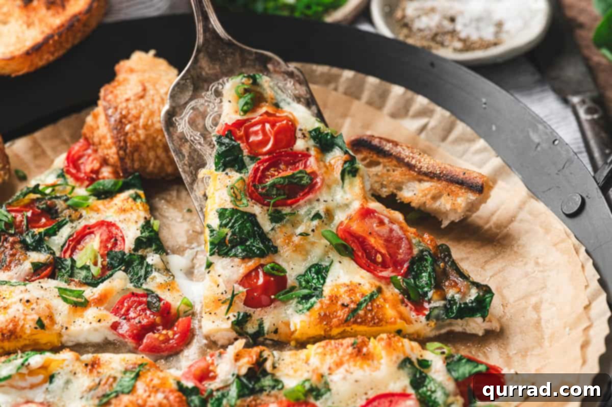 Fluffy Air Fryer Egg Frittata 8 Close-up shot of a savory frittata slice being lifted with a serving spatula, revealing layers of gooey melted cheese, vibrant tomatoes, and fresh spinach nestled within the fluffy egg.