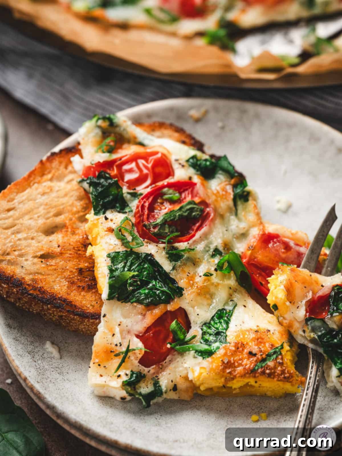 Fluffy Air Fryer Egg Frittata 9 Close-up shot of a savory frittata slice being lifted with a serving spatula, revealing layers of gooey melted cheese, vibrant tomatoes, and fresh spinach nestled within the fluffy egg, ready for enjoyment.
