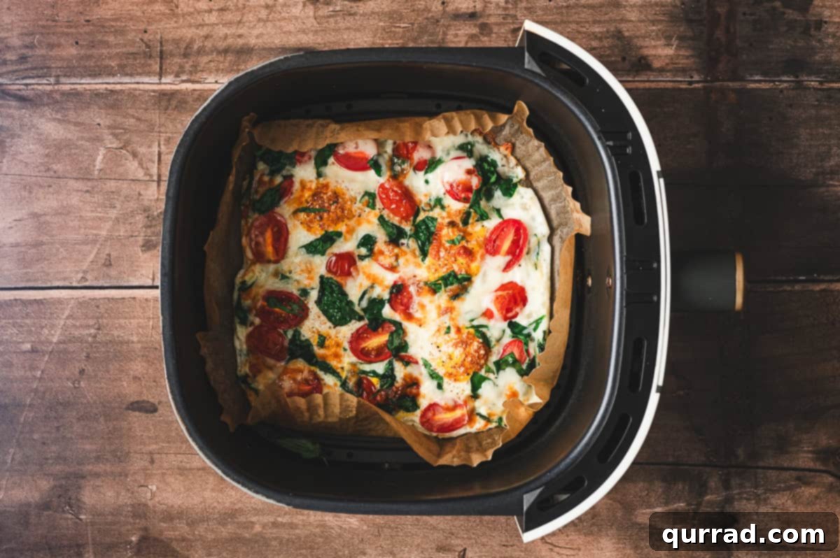 Fluffy Air Fryer Egg Frittata 6 A perfectly cooked air fryer frittata inside the basket, showcasing a golden, puffed texture with beautifully melted cheese and tender vegetables, straight from the air fryer.