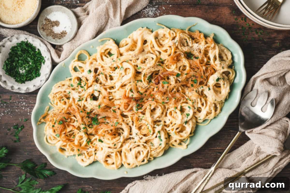 Golden Caramelized Onion Pasta 8 Large serving platter filled with caramelized onion pasta, topped with extra onions and parsley, with small bowls of Parmesan, parsley, and seasonings on the side.