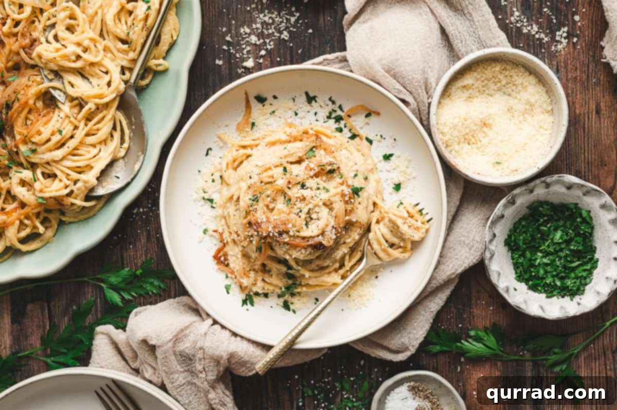 Golden Caramelized Onion Pasta 9 A white plate of creamy caramelized onion pasta twirled with a fork, topped with Parmesan and parsley, with extra grated cheese and herbs in small bowls nearby.