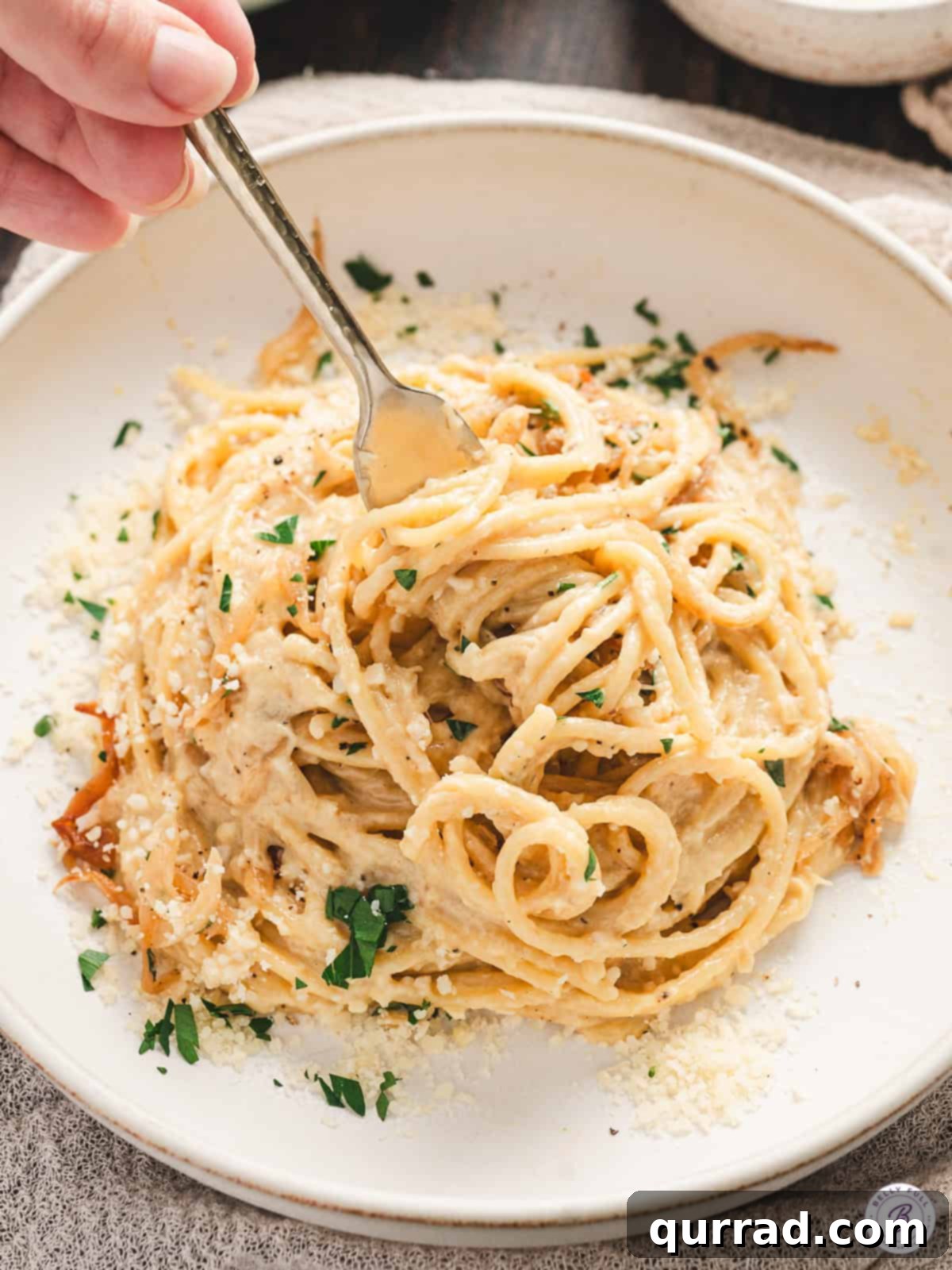 Golden Caramelized Onion Pasta 10 Close-up of creamy caramelized onion pasta on a green serving platter, garnished with fresh parsley and black pepper, with a spoon and fork ready for serving.