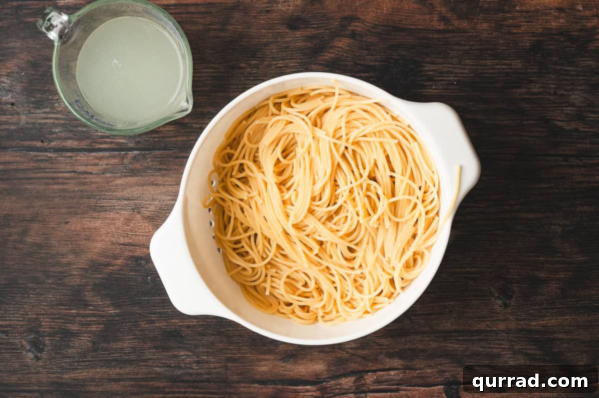Golden Caramelized Onion Pasta 5 Cooked spaghetti drained in a white colander with a measuring cup of reserved starchy pasta water on the side.