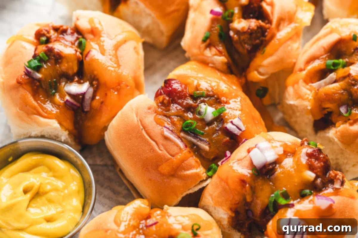 Bite-Sized Chili Cheese Dogs 7 Golden mini chili cheese dogs arranged on a tray, garnished with fresh scallions and red onion, served alongside a bowl of mustard.