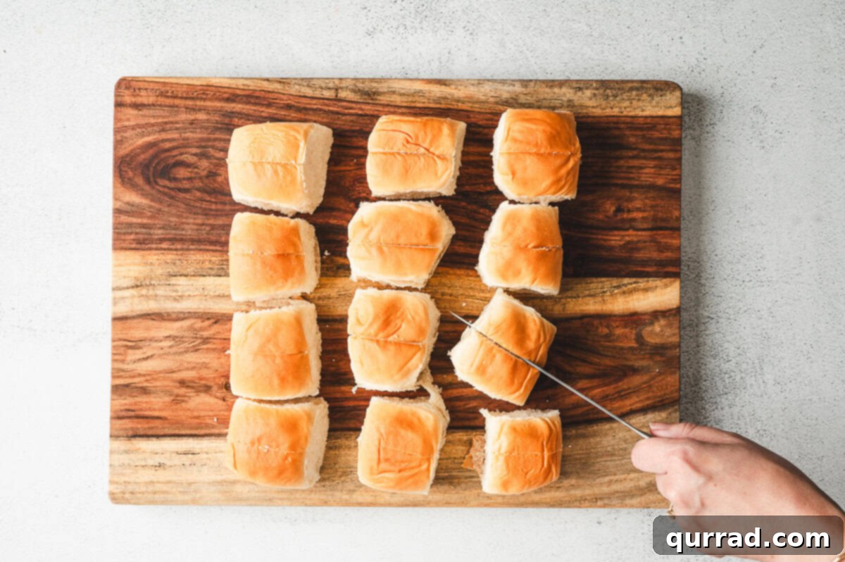 Bite-Sized Chili Cheese Dogs 3 Sweet Hawaiian rolls being separated and sliced down the center on a wooden cutting board with a knife, demonstrating the first step in preparing the mini chili cheese dogs.