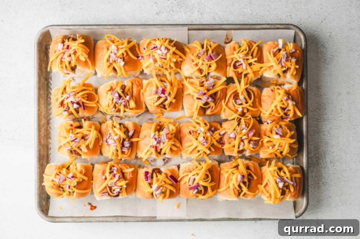 Bite-Sized Chili Cheese Dogs 5 Mini chili dogs generously topped with shredded cheddar cheese and finely diced red onion, awaiting their final bake in the oven.