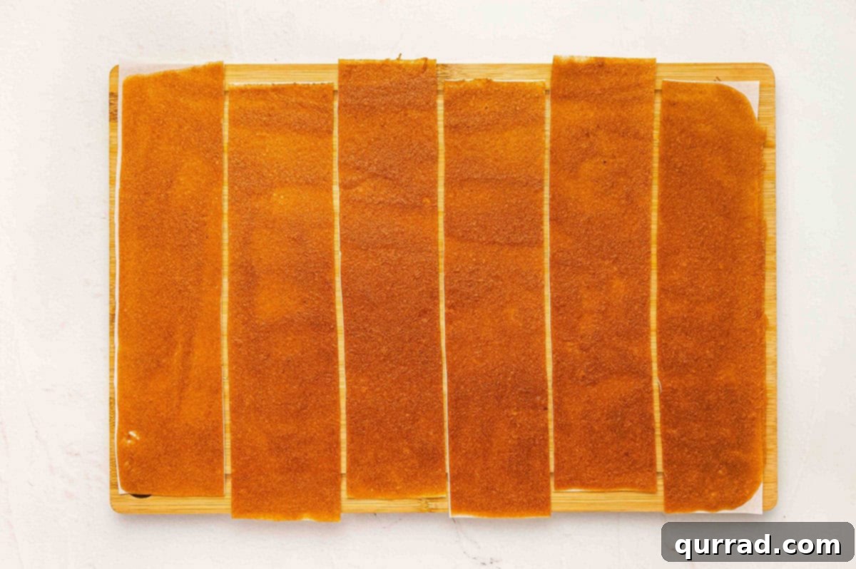 Apple fruit leather cut into long strips on a cutting board, ready to roll.