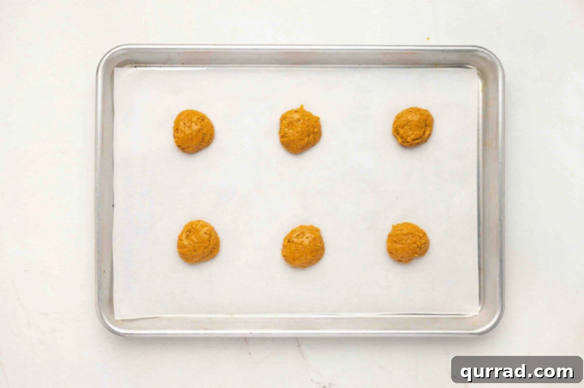 Creamy Pumpkin Harvest Cookies 8 A baking sheet lined with parchment paper with six spoonfuls of pumpkin batter evenly spaced apart.