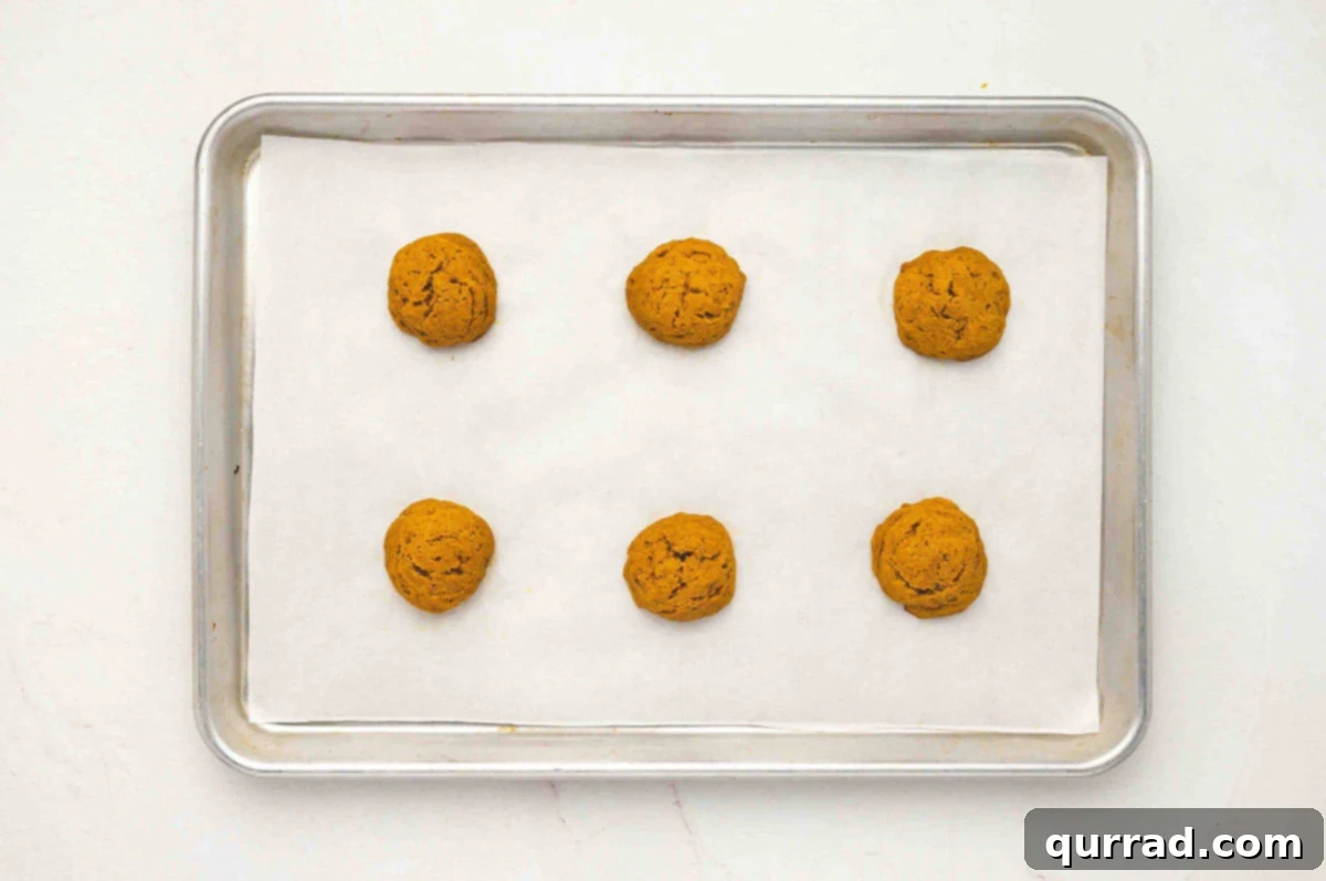 Creamy Pumpkin Harvest Cookies 9 A baking sheet lined with parchment paper holding six baked pumpkin cake rounds cooling after baking.