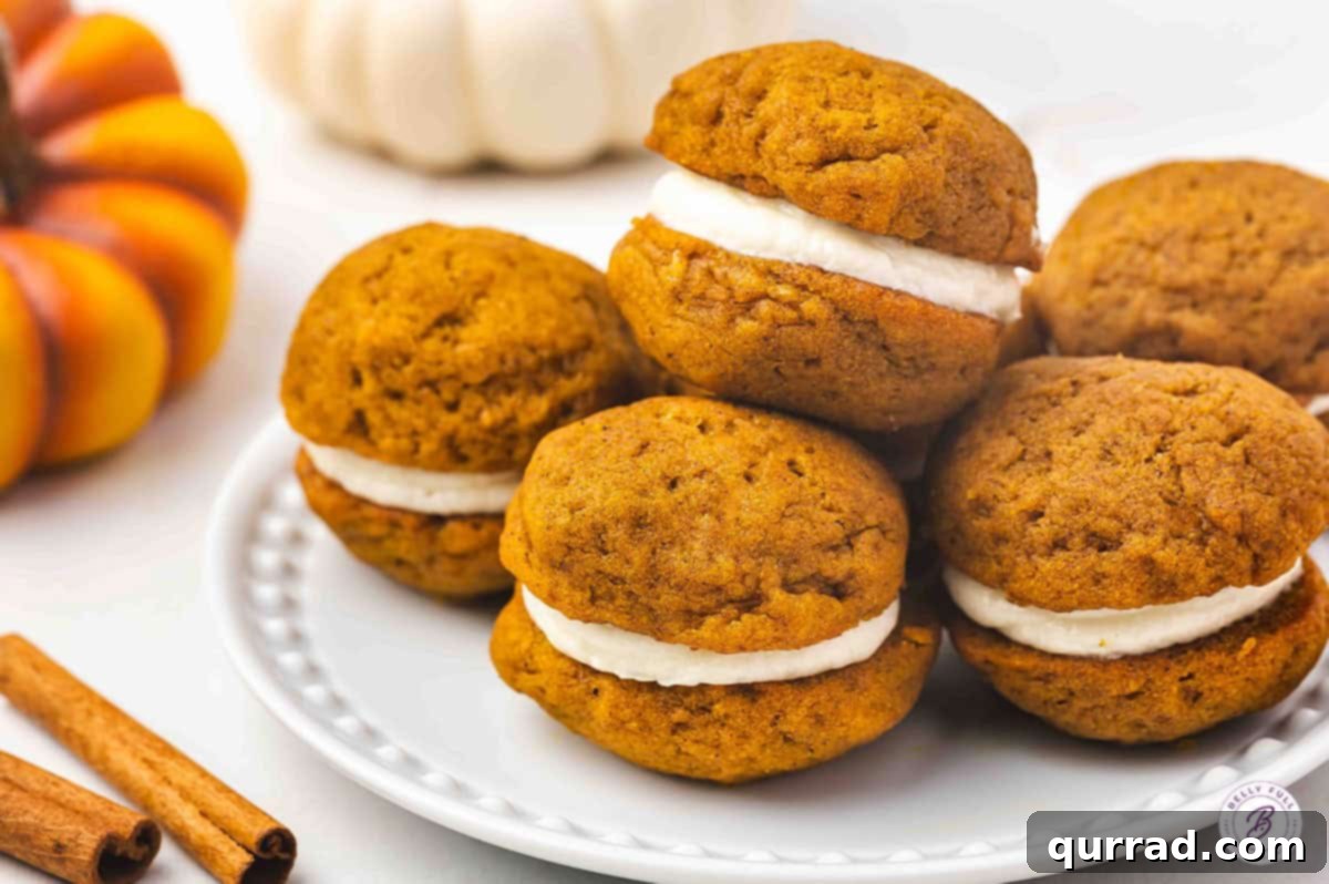 Creamy Pumpkin Harvest Cookies 12 A white plate with pumpkin whoopie pies stacked and ready to serve, surrounded by pumpkins and cinnamon sticks.