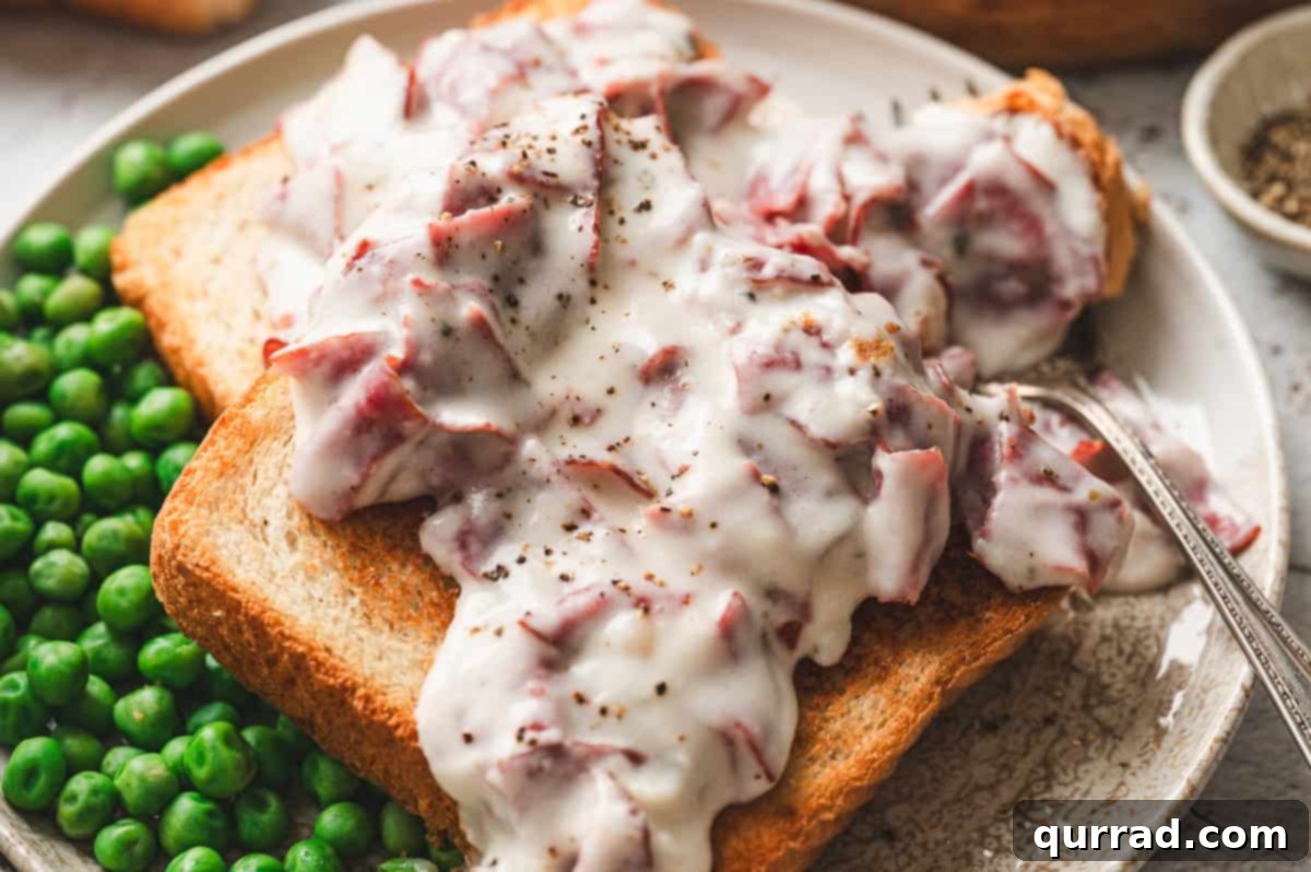 Savory Shredded Beef in Cream Sauce 9 A plate of toast topped with creamed chipped beef, served alongside bright green peas with a fork on the side.