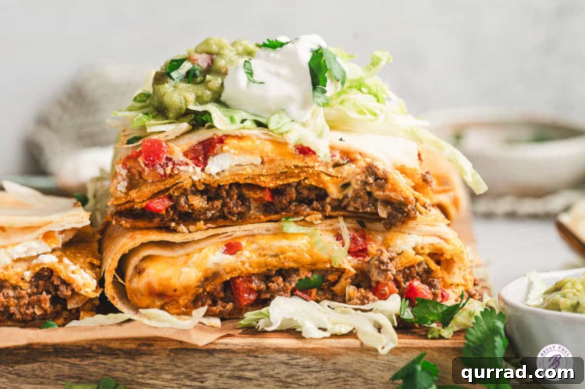 Close-up of stacked slices of Crunchwrap Casserole showing layers of tortillas, beef, cheese, sour cream, and red peppers, topped with lettuce, guacamole, and sour cream.