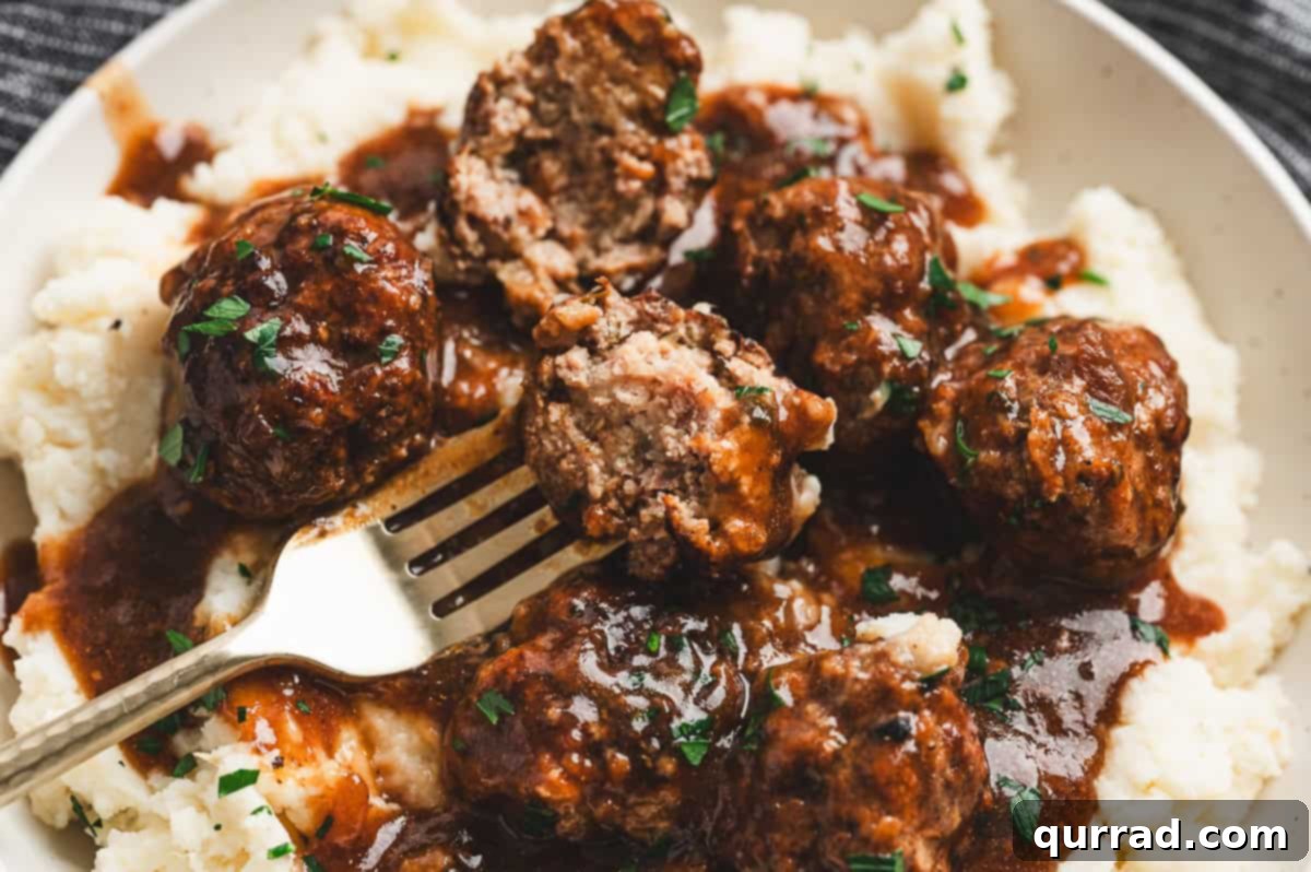 Savory Slow Cooker Salisbury Steak Meatballs 9 A fork cutting into a Salisbury steak meatball, revealing its tender, juicy interior, served over fluffy mashed potatoes with rich brown gravy and garnished with fresh parsley.