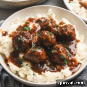 Bowl of Salisbury steak meatballs served over mashed potatoes, topped with rich brown gravy and fresh parsley.