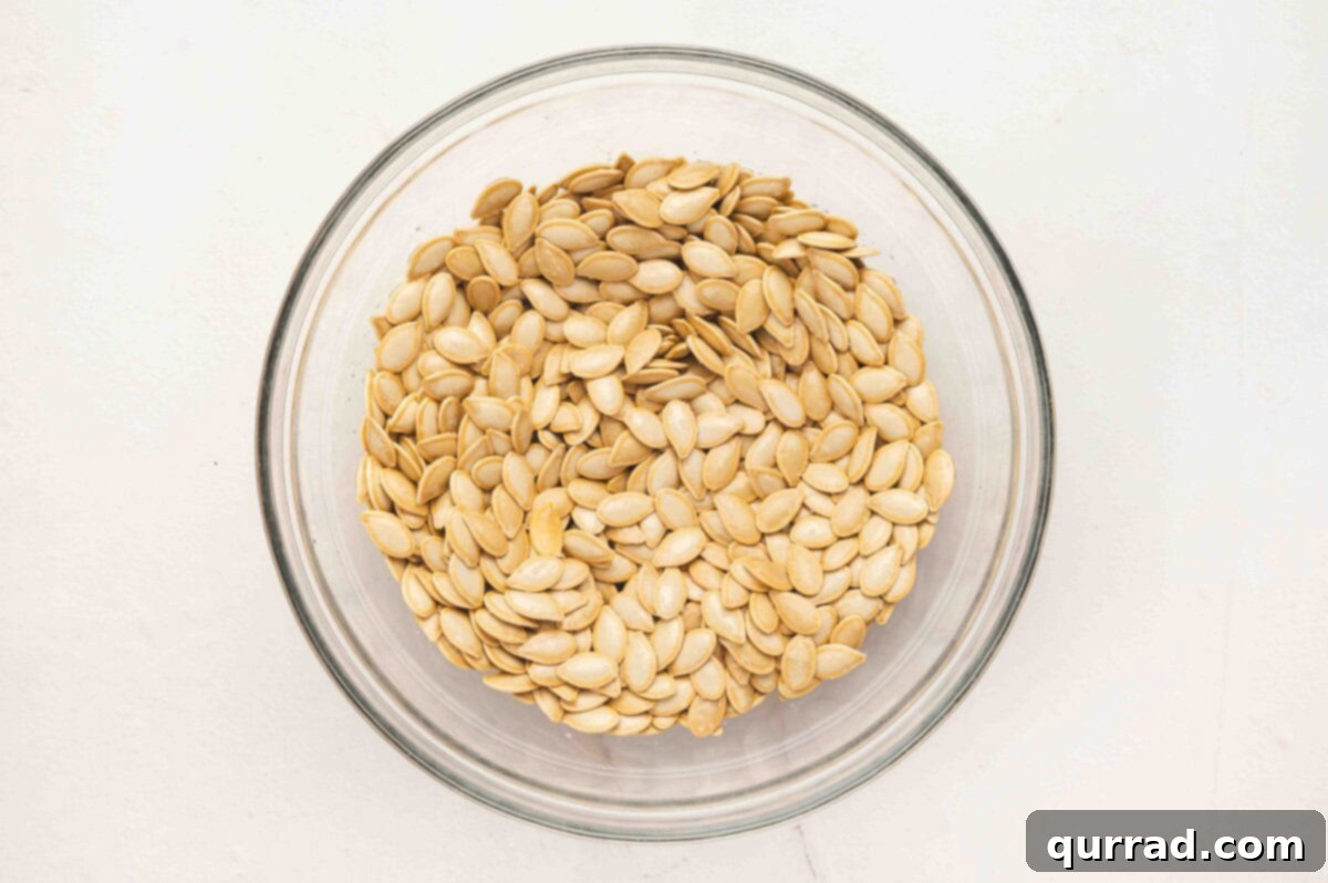 Clean, soaked pumpkin seeds resting in a clear glass bowl after rinsing, ready for drying.