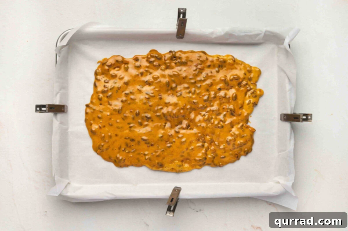 Hot pumpkin seed brittle mixture spread out evenly on a parchment-lined baking sheet to cool.