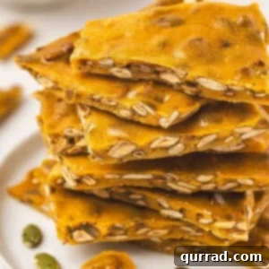 Stack of golden pumpkin seed toffee brittle pieces on a white plate with pumpkin seeds scattered around.