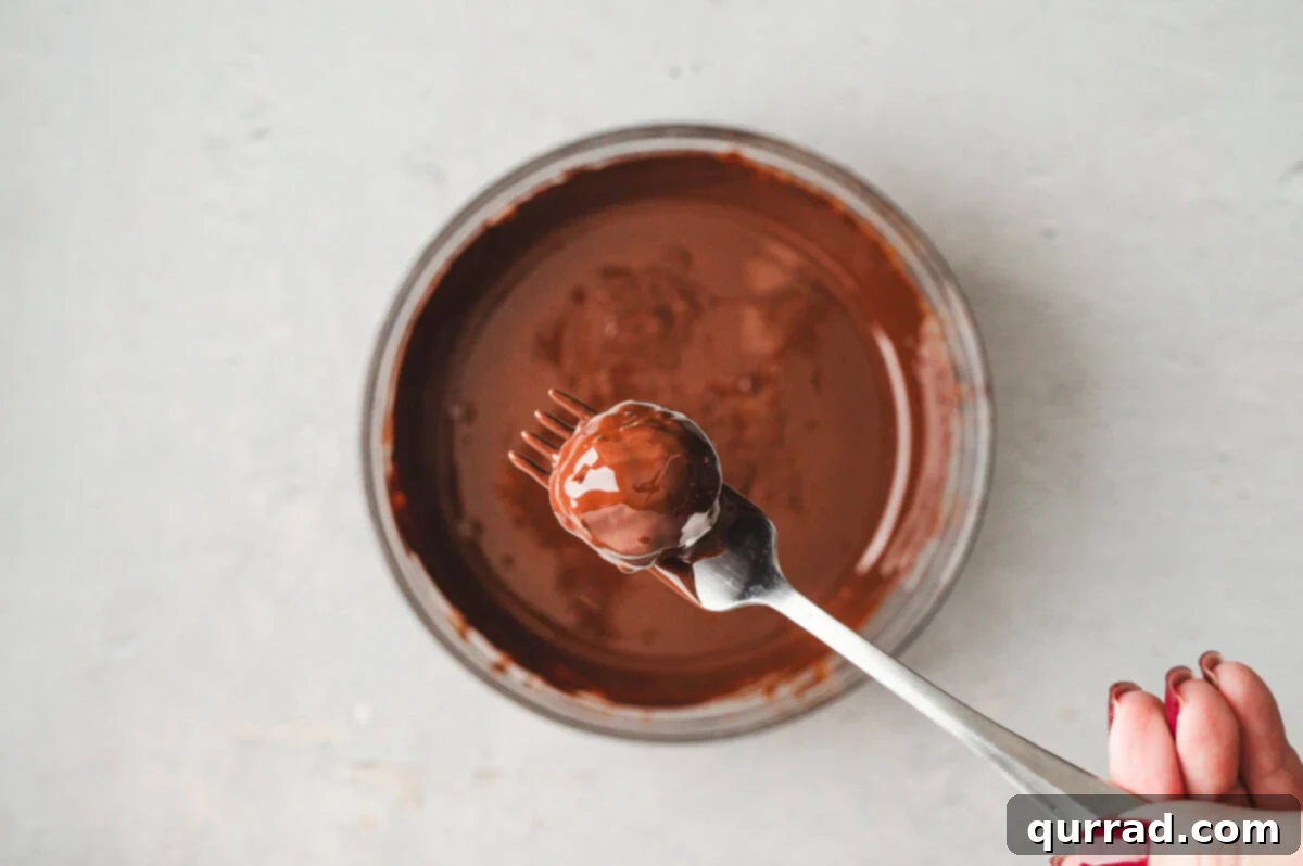 Decadent Dubai Truffles 9 A fork holding one kataifi truffle being dipped into glossy melted dark chocolate.