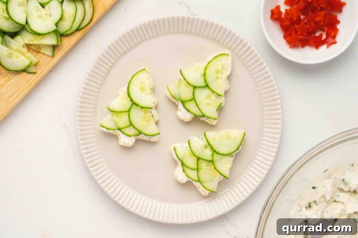 Christmas Tree Cucumber Bites 9 Partially assembled Christmas tree sandwiches on a plate with cucumber slices and bell pepper pieces nearby