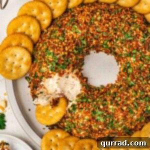 Christmas wreath cheese ball coated in chopped almonds, sun-dried tomatoes, and parsley, arranged in a wreath shape and served with round butter crackers on a platter, with a portion scooped out.
