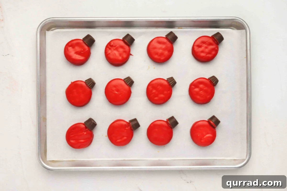 Ritz Cracker Holiday Charms 6 Red-dipped Ritz cookies on a baking sheet with Rolos attached on top to look like Christmas ornament hooks.