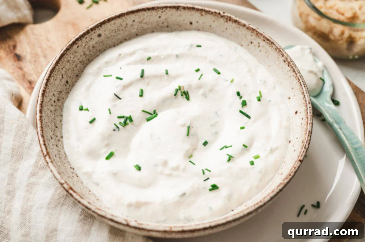 Horseradish Cream 5 Close-up view of creamy horseradish sauce in a speckled bowl, garnished with chopped chives.
