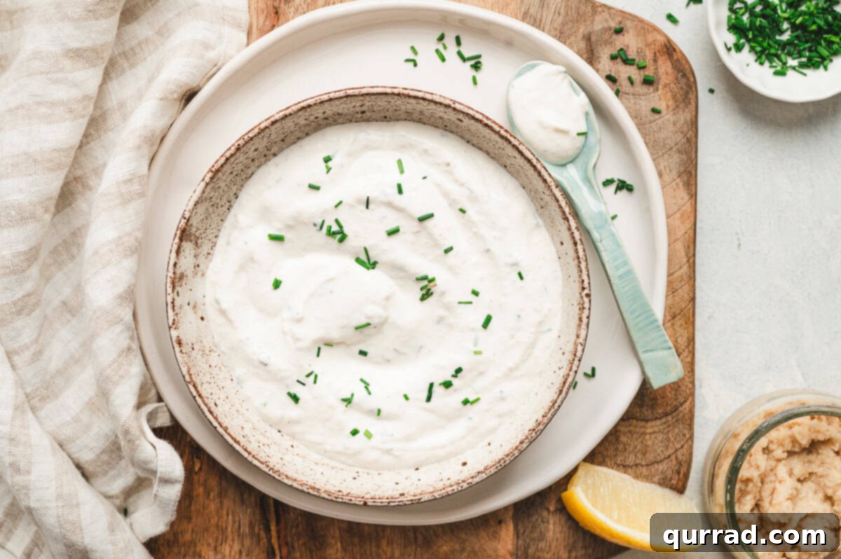 Horseradish Cream 6 Overhead shot of horseradish sauce in a bowl with chives, a spoon, lemon wedge, and fresh horseradish jar on a wooden board.