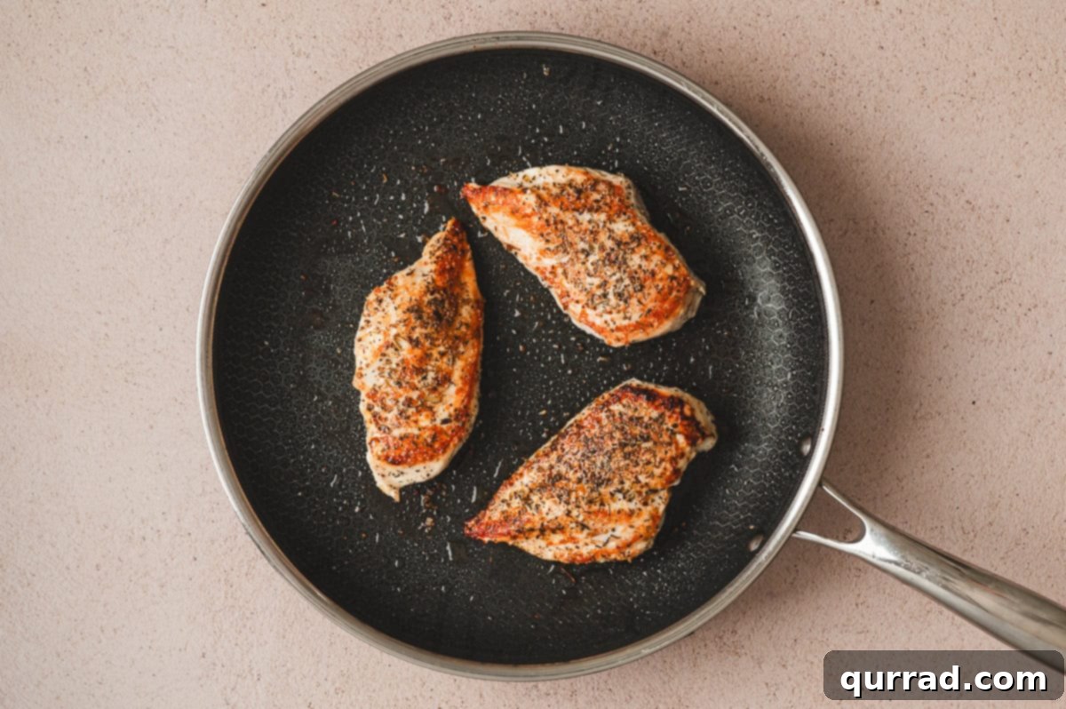 Seasoned chicken breasts searing in a skillet until golden brown
