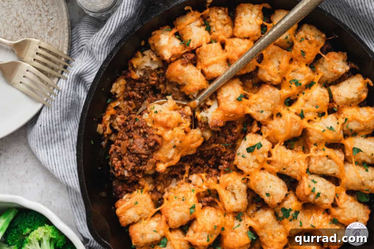 Spoon scooping Sloppy Joe Tater Tot Casserole from a skillet.