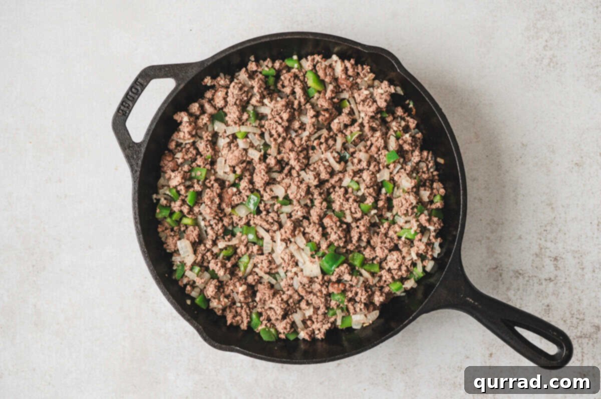 Ground beef browning with diced onion and green bell pepper in a skillet.
