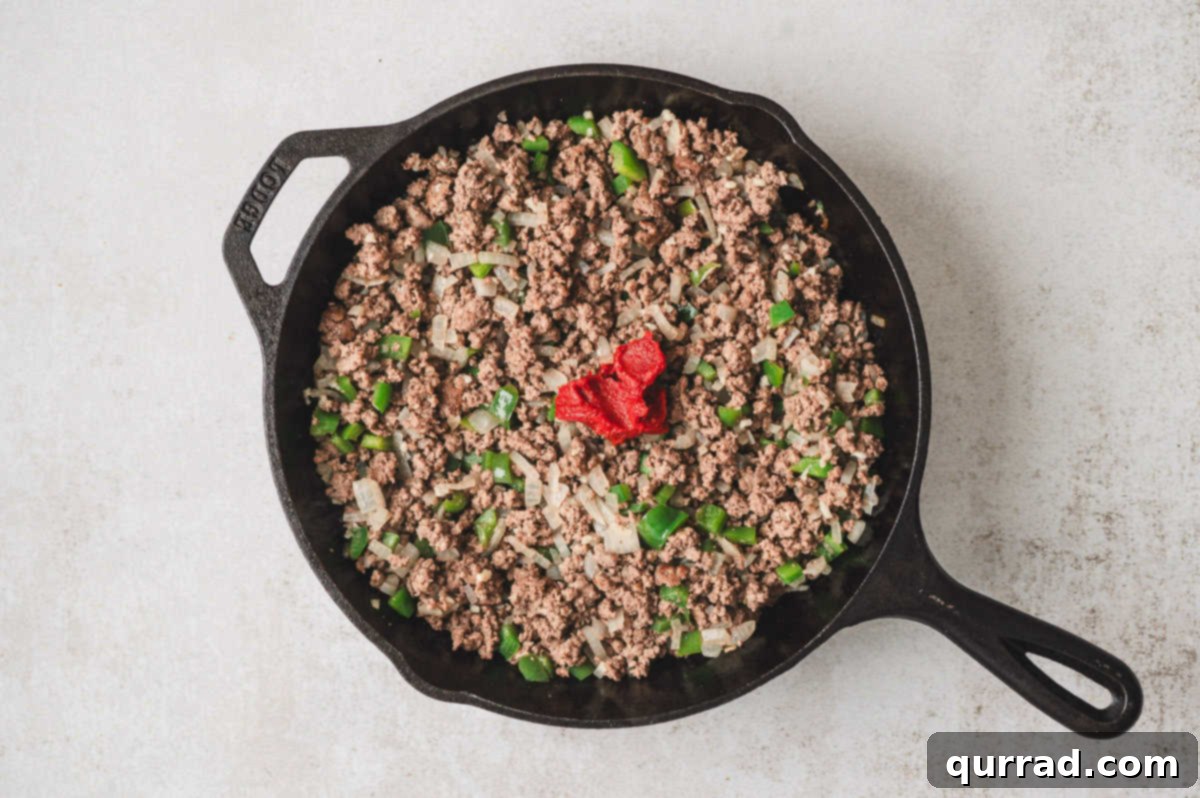 Tomato paste added to browned ground beef mixture in a skillet.