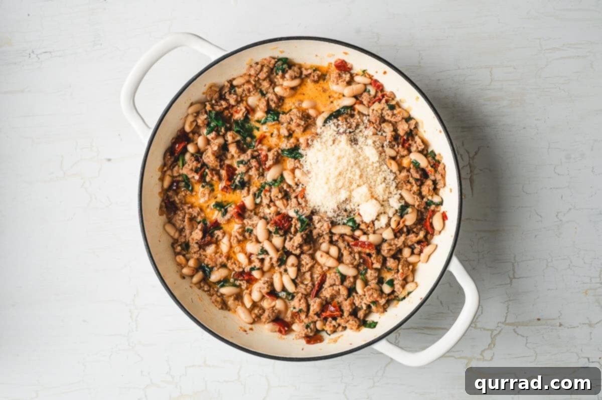 Tuscan Sausage and White Bean Skillet 7 Cooked sausage and beans mixture in a skillet topped with a mound of freshly grated Parmesan cheese before stirring.