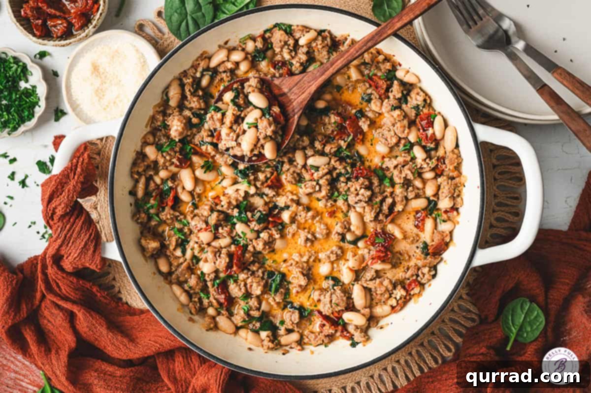 Tuscan Sausage and White Bean Skillet 8 Large white skillet filled with Tuscan white bean and sausage mixture, garnished with parsley, surrounded by bread, cheese, and plates on the table.