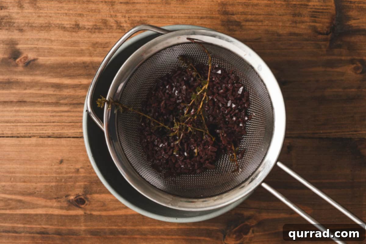 Velvety Red Wine Glaze 8 Straining the reduced red wine sauce through a fine mesh sieve to remove the cooked shallots, garlic, and herbs.