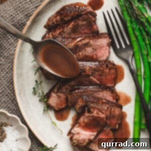 Velvety Red Wine Glaze 3 Sliced medium-rare steak on a plate with asparagus, topped with homemade red wine sauce being spooned over the meat.