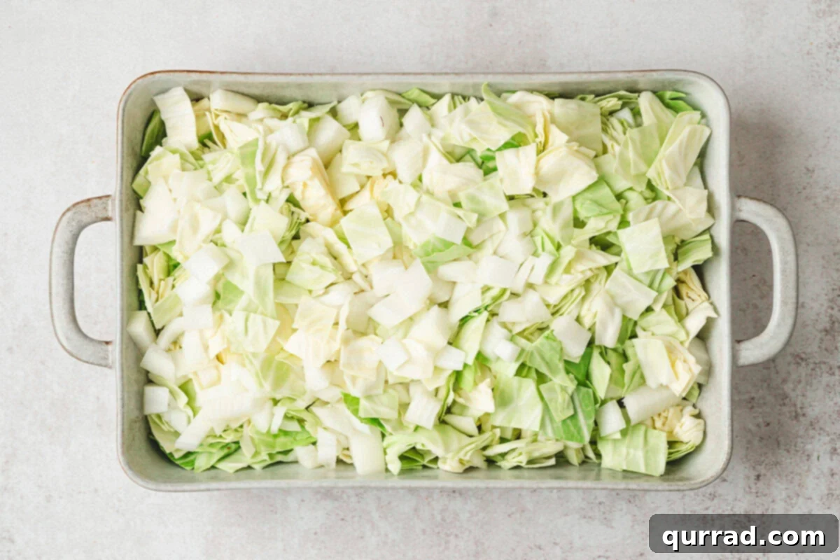 Chopped green cabbage and yellow onion placed in a greased baking dish, ready for the next layer.