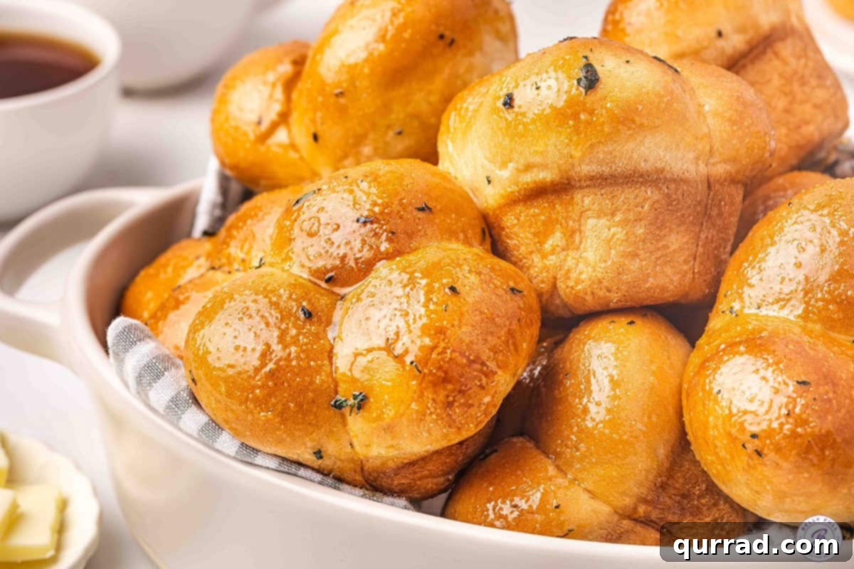 Golden Pull-Apart Buns 10 Several homemade cloverleaf rolls arranged on a pristine white plate, elegantly garnished with a sprig of fresh thyme, perfectly ready to be served and enjoyed.